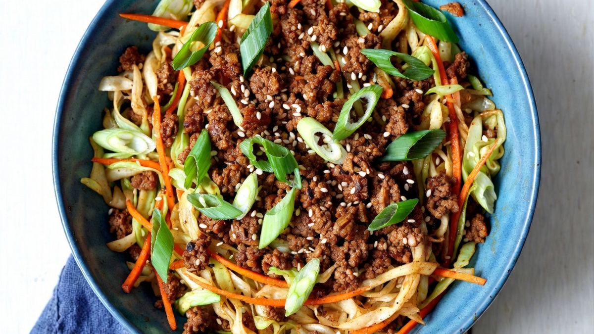 Egg roll in a bowl served in a blue ceramic bowl with browned ground beef, tender-crisp cabbage, green onions, and sesame oil sauce