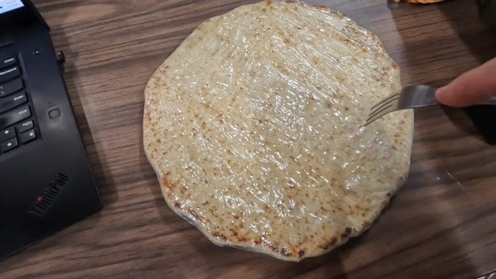 Fork poking holes in frozen pizza crust through plastic wrap before cooking